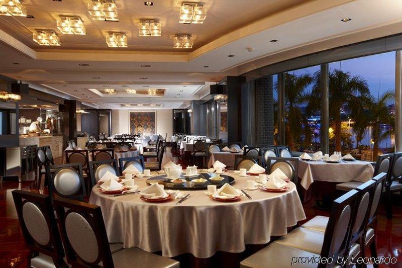 Ambassador Hotel Гаосюн Экстерьер фото The photo depicts an elegant restaurant interior. It features round tables, each covered with white tablecloths and set with dishes and utensils, suggesting a formal dining experience. The restaurant has a modern and sophisticated design, with a well