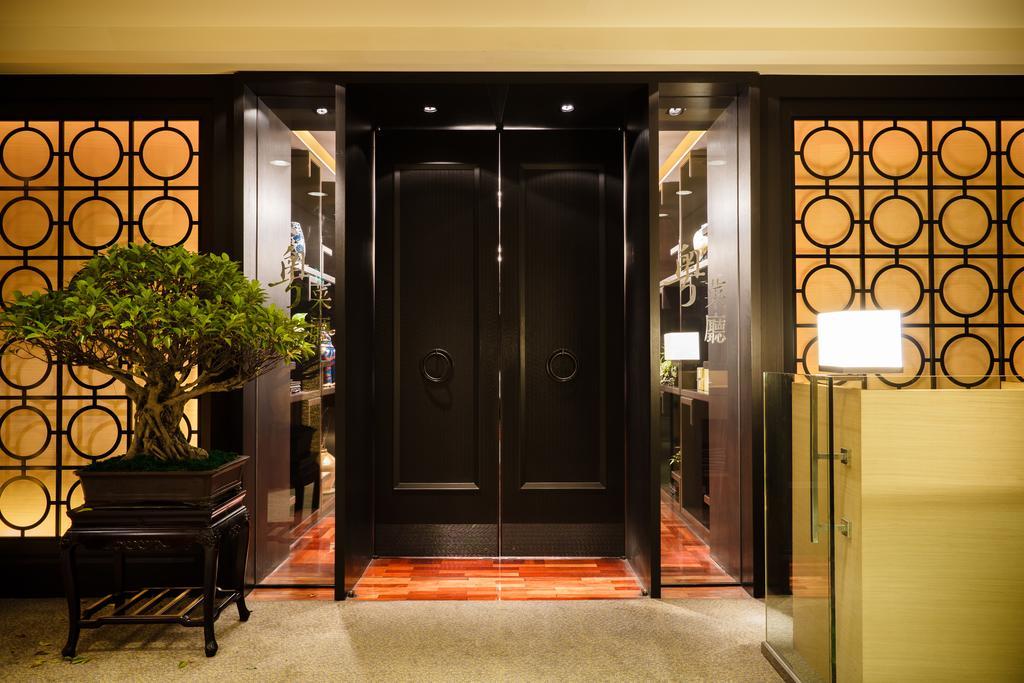 Ambassador Hotel Гаосюн Экстерьер фото The photo shows an elegant entrance area featuring a set of large black double doors, which appear to be a main entryway. The walls surrounding the doors have a decorative design with circular patterns. On one side, there is a small tree in a planter