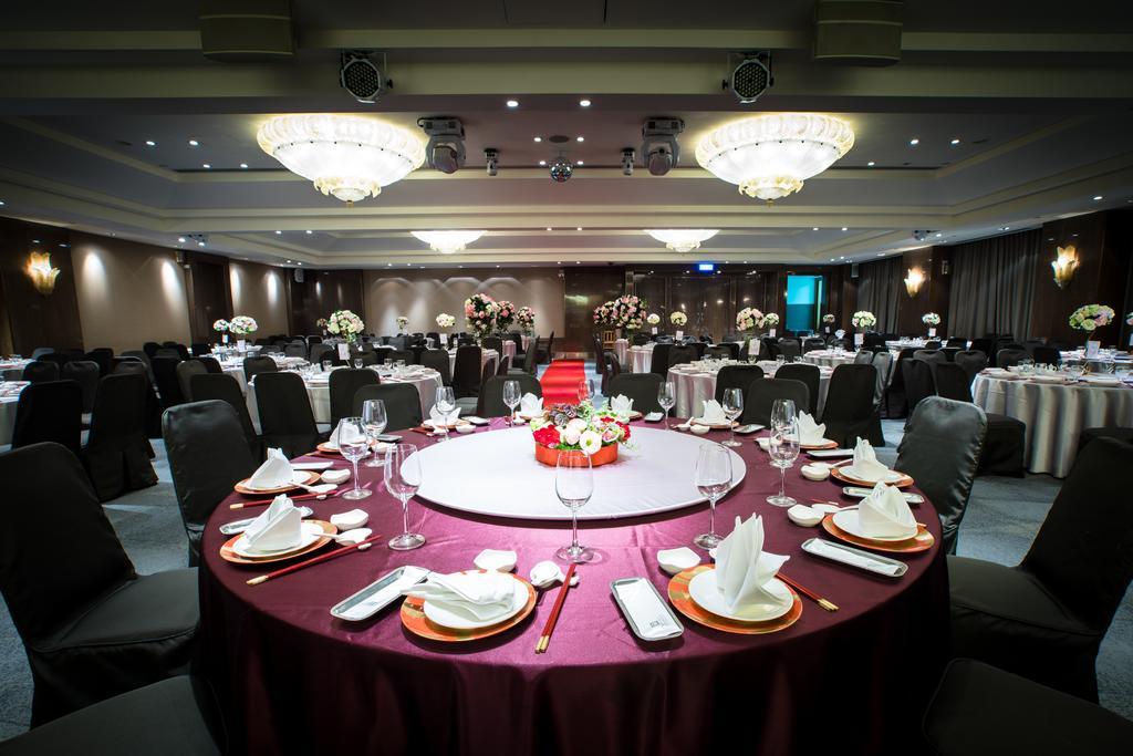 Ambassador Hotel Гаосюн Экстерьер фото The photo depicts an elegantly set dining area for an event. 

In the foreground, there is a circular table covered with a dark red tablecloth, featuring a centerpiece of flowers in vibrant colors. The table is equipped with white plates, polished cu