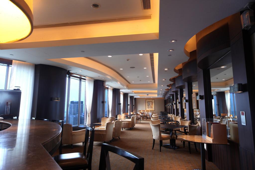 Ambassador Hotel Гаосюн Экстерьер фото The photo shows the interior of a modern restaurant or lounge. The space features elegant seating with cream-colored chairs and wooden tables, arranged in a spacious layout. Soft, warm lighting highlights the architectural details of the ceiling and 