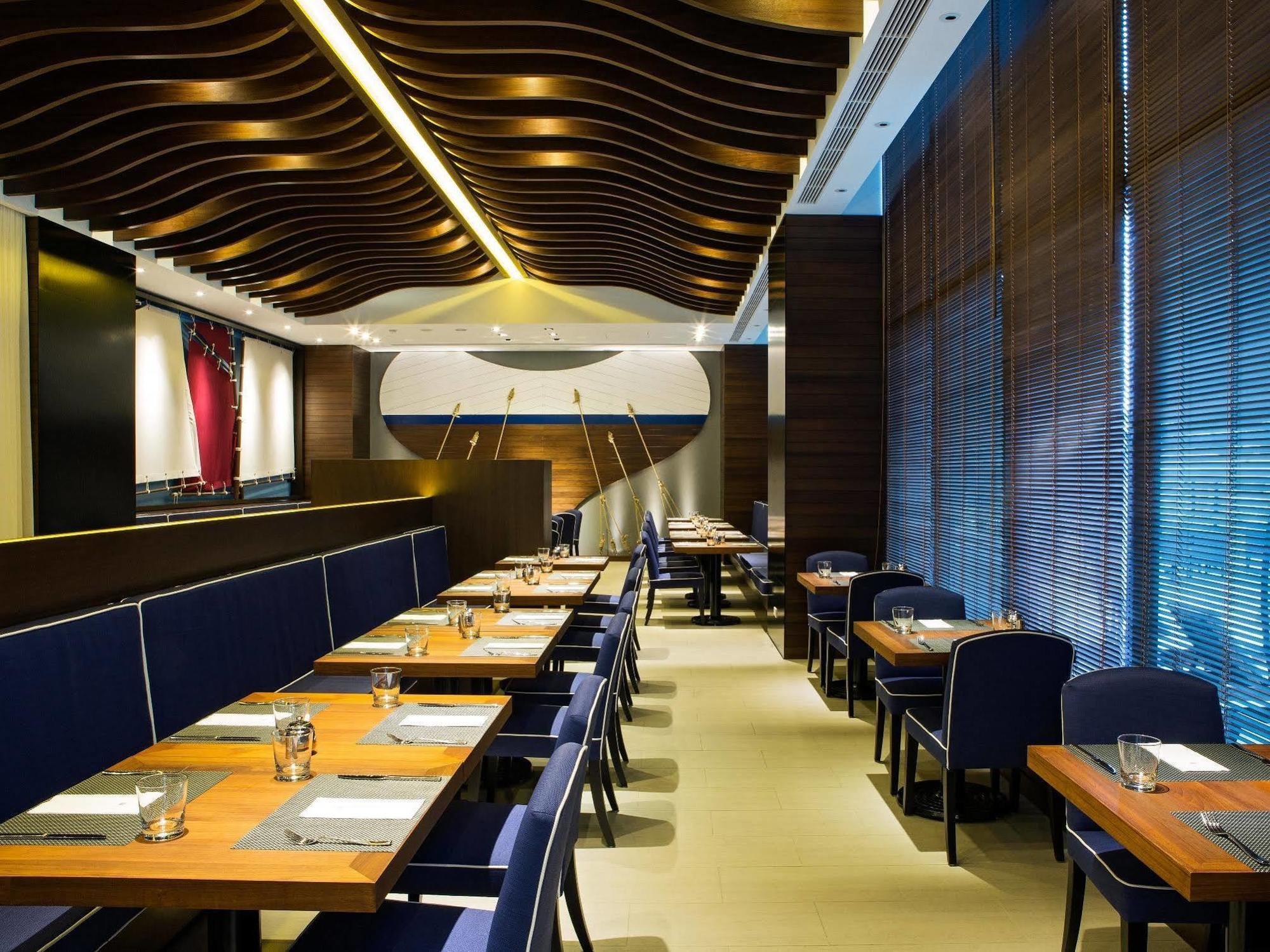 Ambassador Hotel Гаосюн Экстерьер фото The photo shows the interior of a modern restaurant. It features wooden flooring and stylish seating arrangements with tables. The tables are set with menus, cutlery, and glasses, indicating a dining setup. The walls are adorned with contemporary des