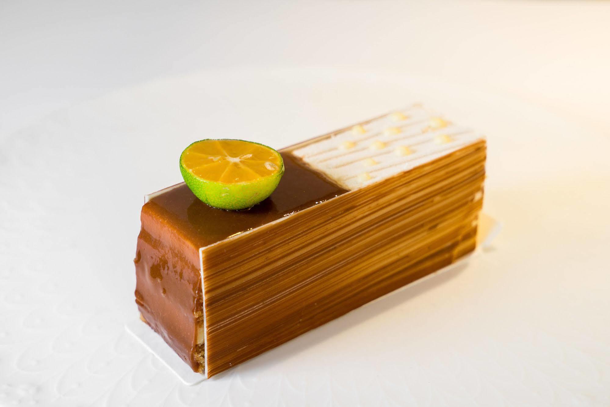 Ambassador Hotel Гаосюн Экстерьер фото The photo shows a dessert that is shaped like a rectangular block or loaf. It features a glossy, golden-brown exterior, likely made with layers of chocolate or caramel. Atop the dessert, there is a halved lime slice, adding a pop of color and suggest