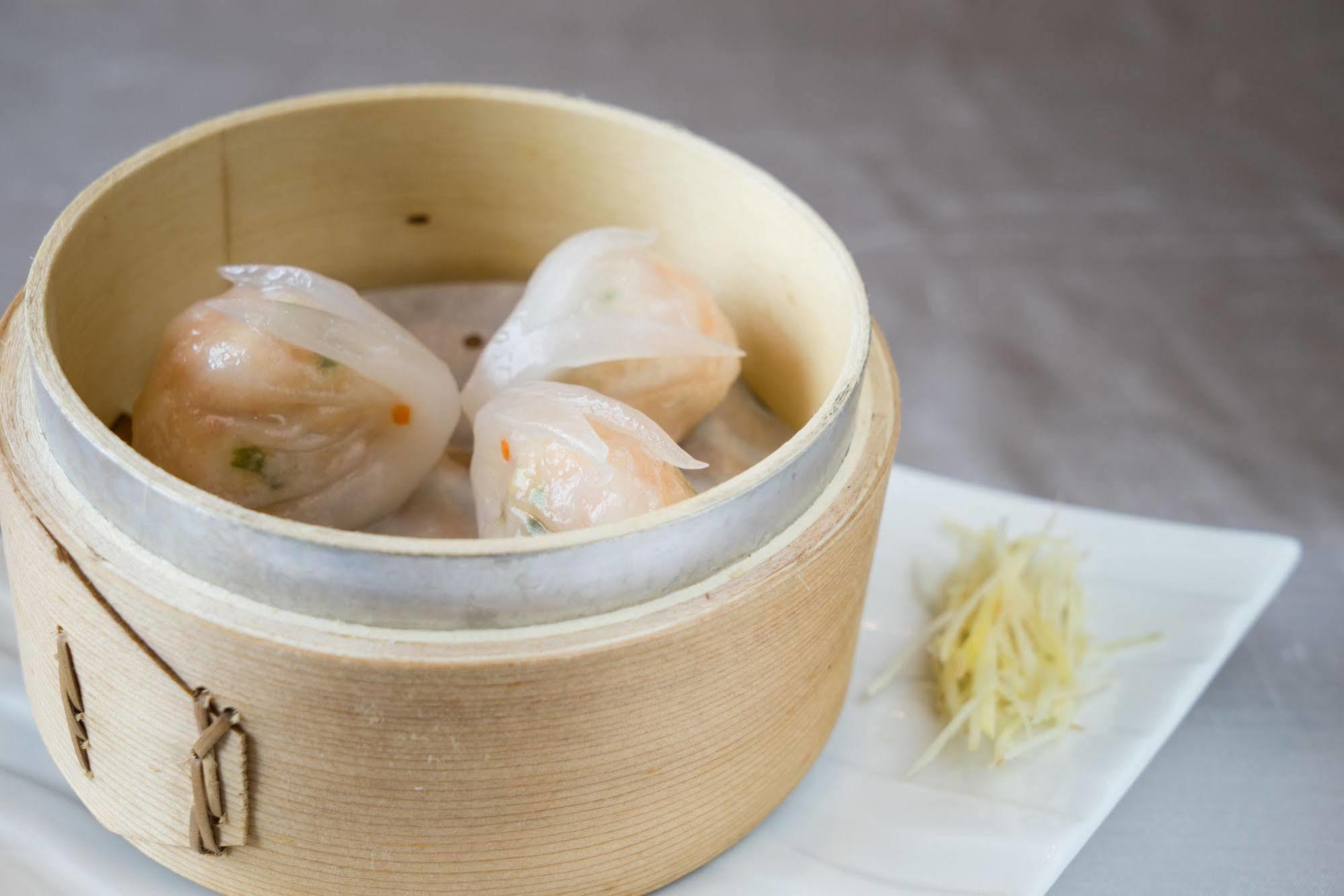 Ambassador Hotel Гаосюн Экстерьер фото The photo shows a wooden steamer basket containing three pieces of dumplings, likely shrimp dumplings known as har gow. These dumplings are translucent, revealing bits of shrimp and vegetables inside. Next to the steamer, there is a small mound of sl