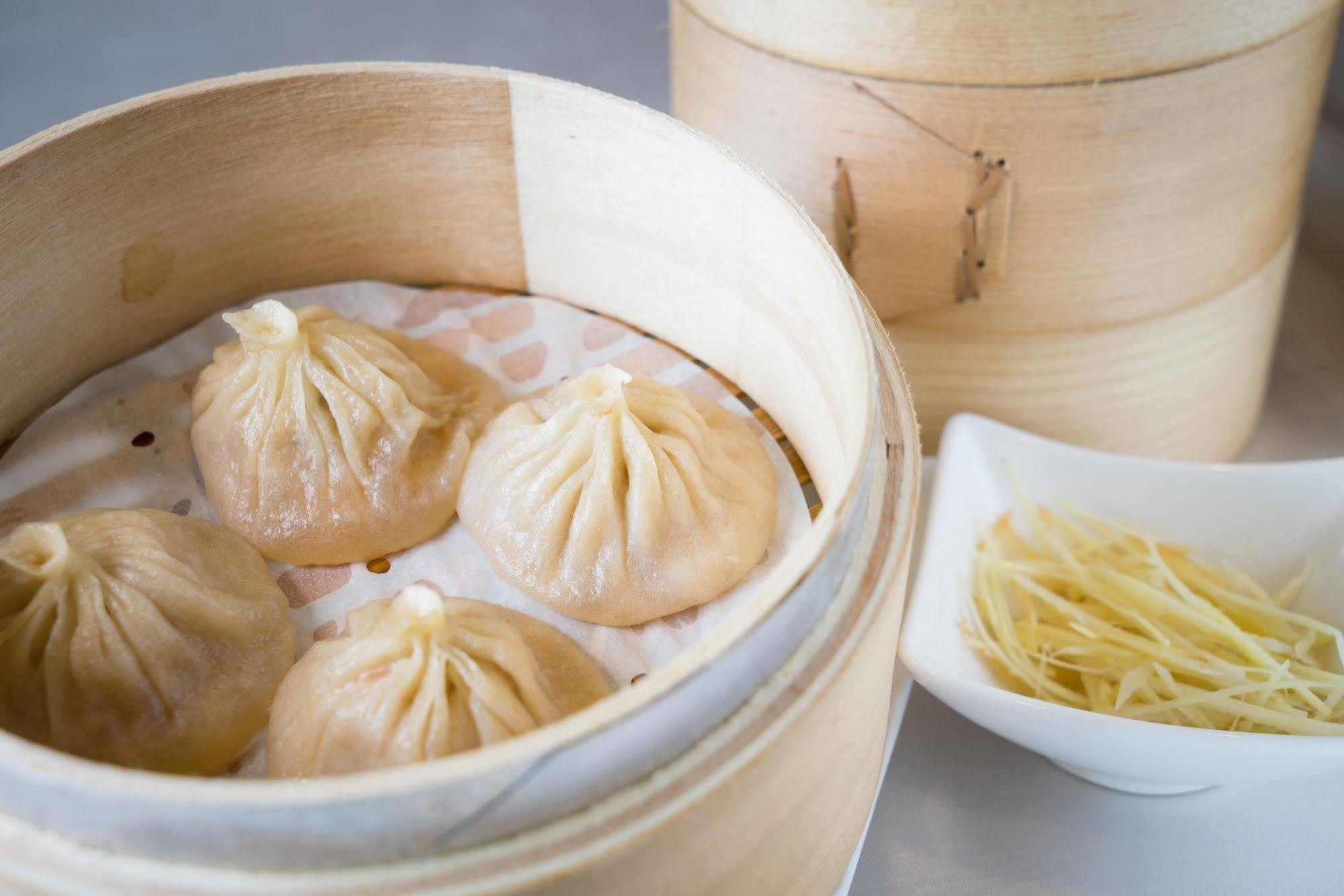 Ambassador Hotel Гаосюн Экстерьер фото The photo shows a bamboo steamer containing several dumplings, known as xiaolongbao, which are soup dumplings traditionally filled with meat and broth. The dumplings are arranged neatly on a layer of parchment paper inside the steamer. Next to the st