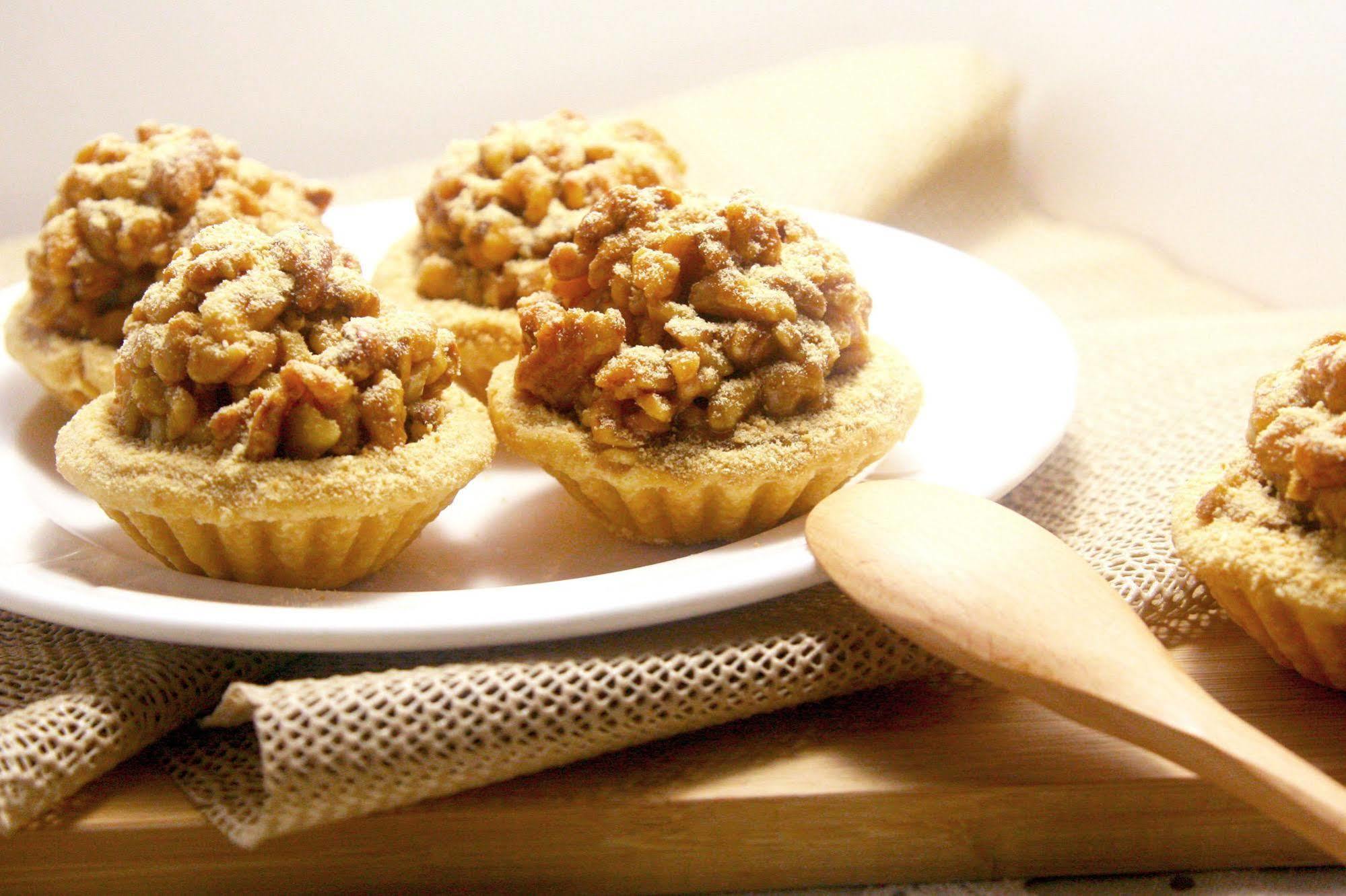 Ambassador Hotel Гаосюн Экстерьер фото The photo shows a plate with small, dessert-like tarts. Each tart features a golden, crumbly crust that is filled with a mixture of chopped nuts and a sweet topping, likely caramelized for added flavor. The tarts are arranged neatly on a white plate,