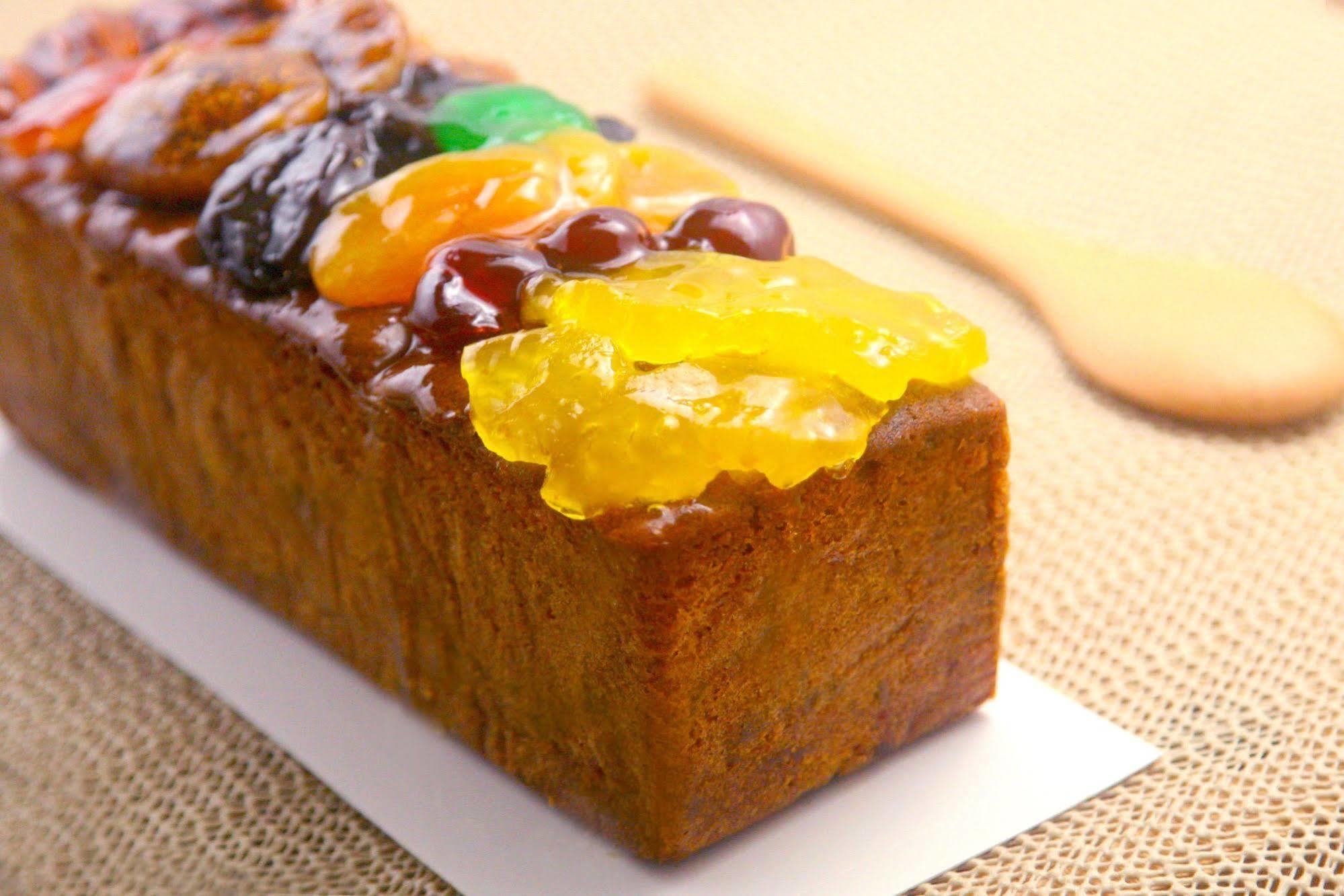 Ambassador Hotel Гаосюн Экстерьер фото The photo shows a rectangular fruitcake that has a rich, dark color and is topped with an assortment of candied fruits. The toppings include brightly colored fruits like orange, green, and yellow, arranged attractively on top of the cake. The texture