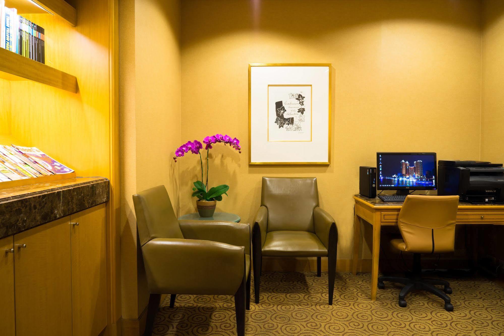 Ambassador Hotel Гаосюн Экстерьер фото The photo shows a cozy corner of a room, which appears to be a waiting or lounge area. There are two stylish chairs positioned near a small table. A potted plant with purple flowers adds a touch of color and freshness to the space. On the wall, there