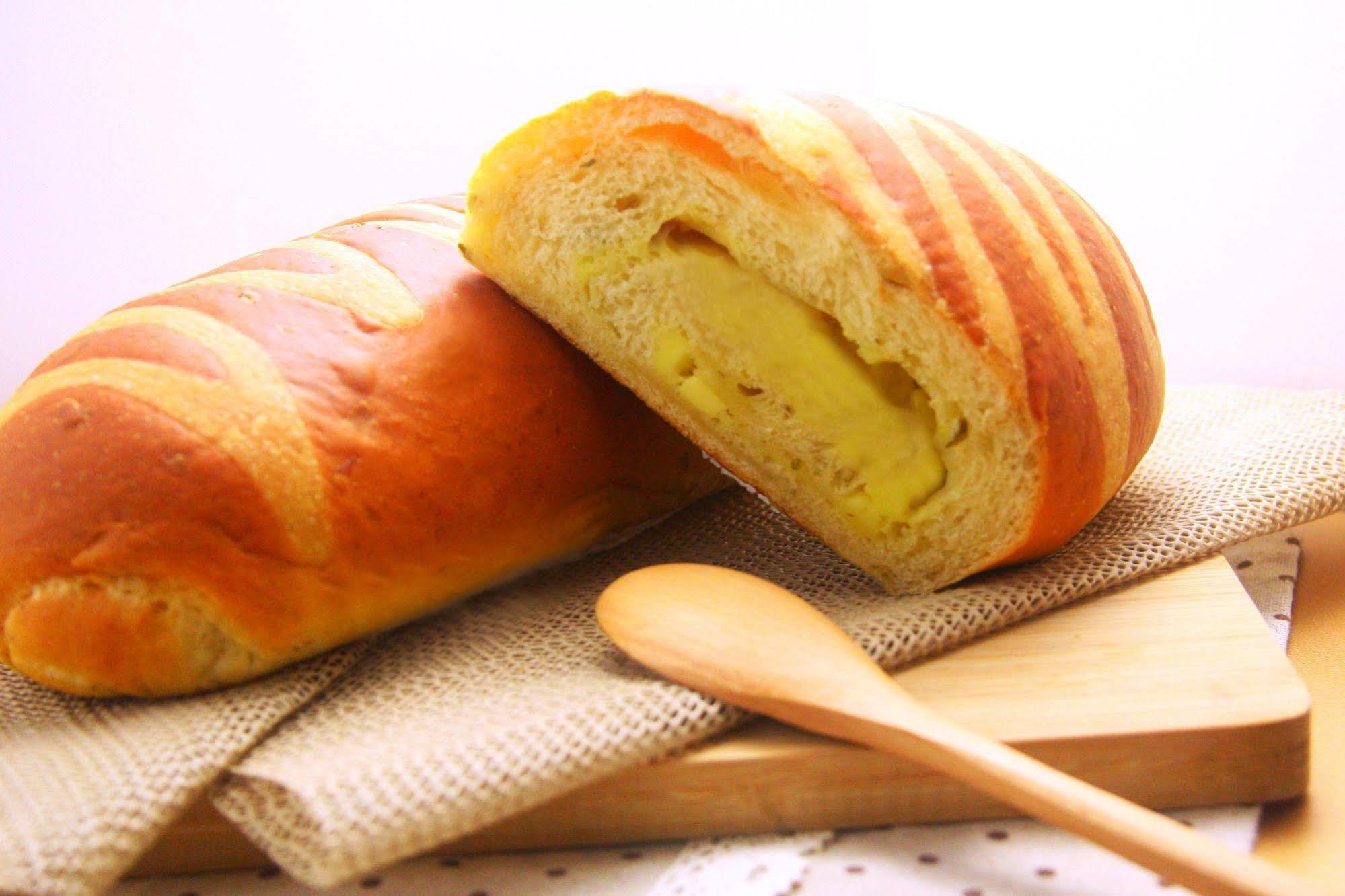 Ambassador Hotel Гаосюн Экстерьер фото The photo shows a loaf of bread that has a golden-brown crust with striped patterns on its surface. One loaf is partially sliced open, revealing a soft, yellow filling inside, which suggests that it might be flavored or sweetened. The bread is placed